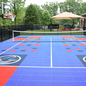 Commercial outdoor multipurpose court with basketball hoops and volleyball net next to a small kids play area.