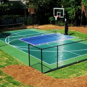 Outdoor multipurpose court with a basketball hoop, a volleyball net and fencing around the court.