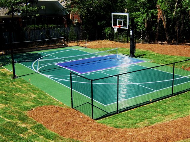 Outdoor multipurpose court with a basketball hoop, a volleyball net and fencing around the court.