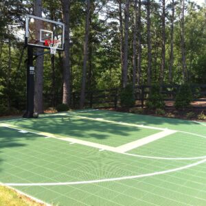 Outdoor basketball court installed in a wooded residential area with one basketball hoop.