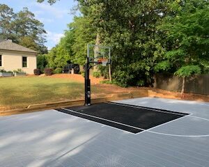Residential outdoor basketball court with gray and black flooring and a house in the background.
