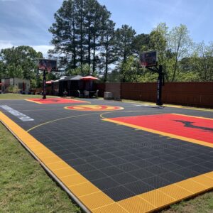 Outdoor residential basketball court with multiple hoops, the Atlanta Hawks branding and a court lighting system.