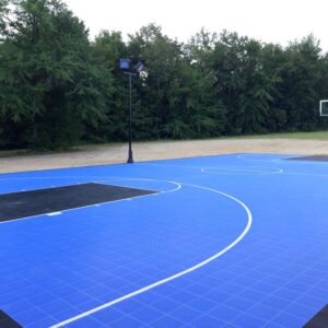 Outdoor basketball court with blue and black court flooring and a court lighting system.