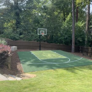 Green outdoor residential basketball court flooring with one hoop in the backyard.